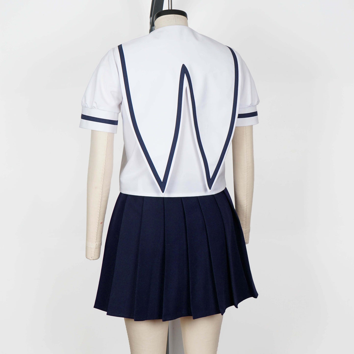Full body shot of a mannequin wearing a white seifuku top with a navy blue jester collar and matching trim on the short sleeves. A dark navy blue skirt is visible beneath the top. The background is a plain white studio backdrop.