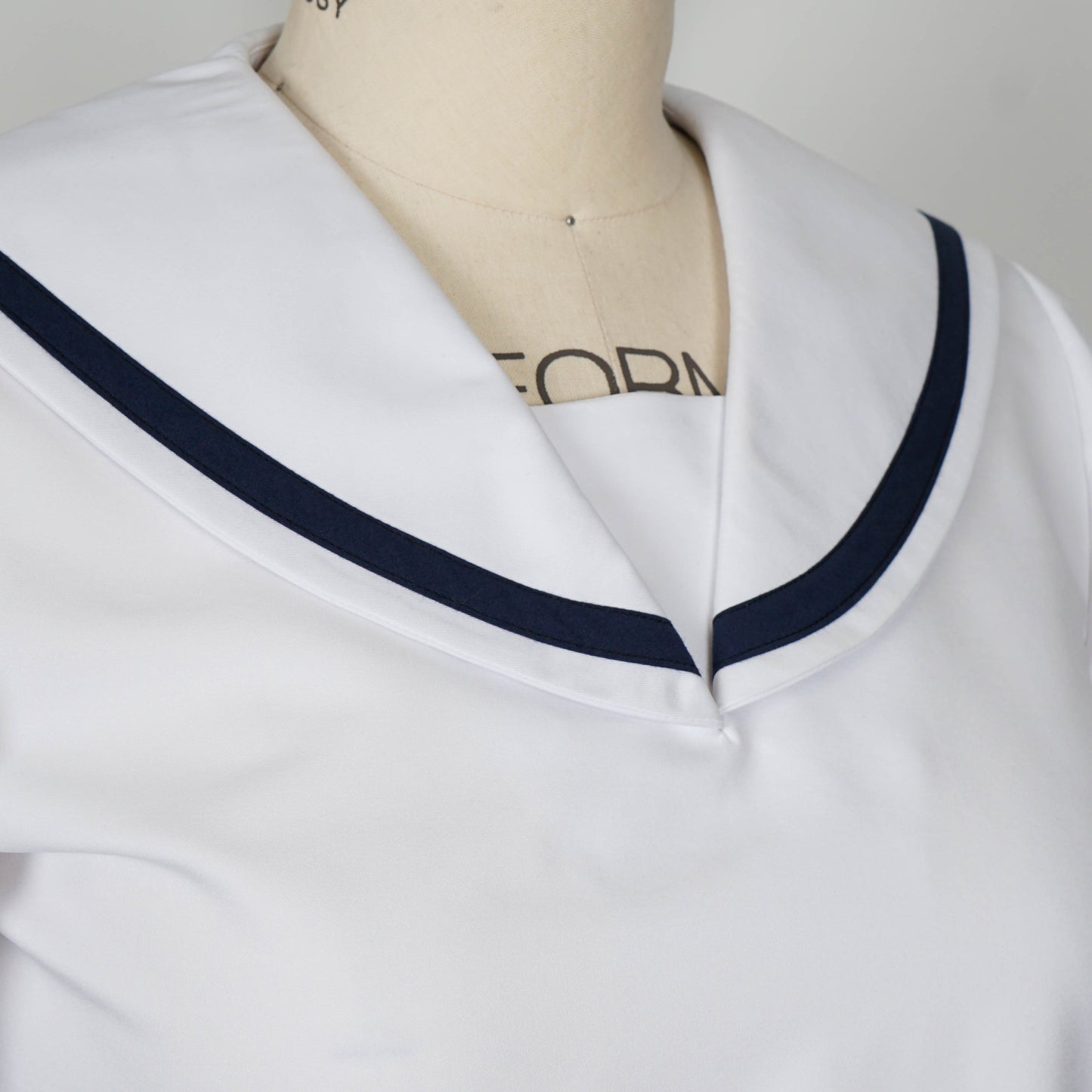Cropped shot showcasing the details of a white seifuku top with a navy blue trimmed sailor collar and short sleeves with matching navy blue trim. The top is displayed on a mannequin.