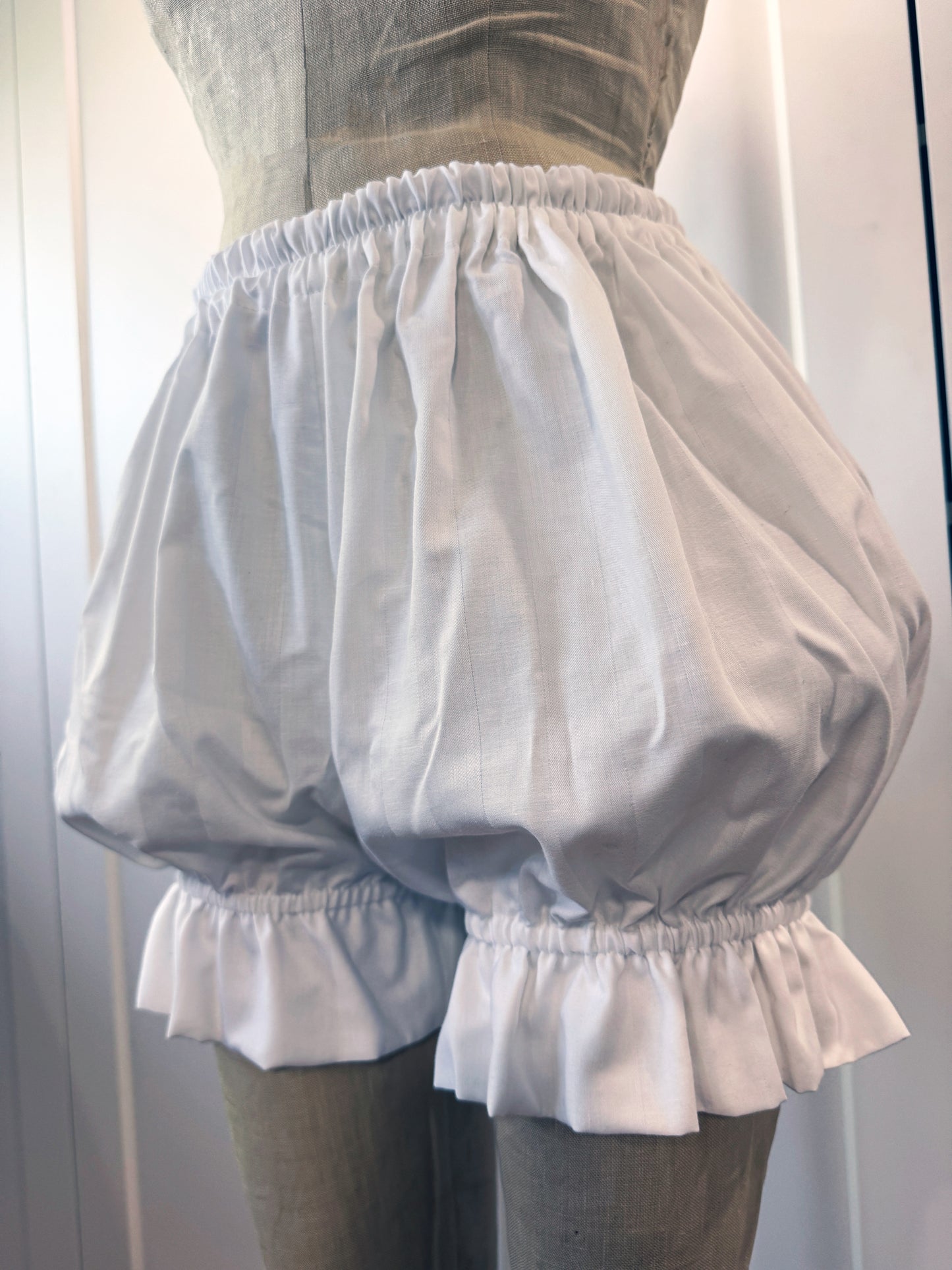 a mannequin displaying a pair of white ruffled shorts gathered at the waist and hems with an elastic