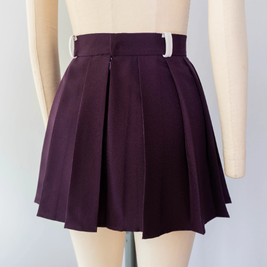 close-up studio shot of a dark purple pleated mini skirt with white belt loops and an invisible zipper shown on a mannequin.
