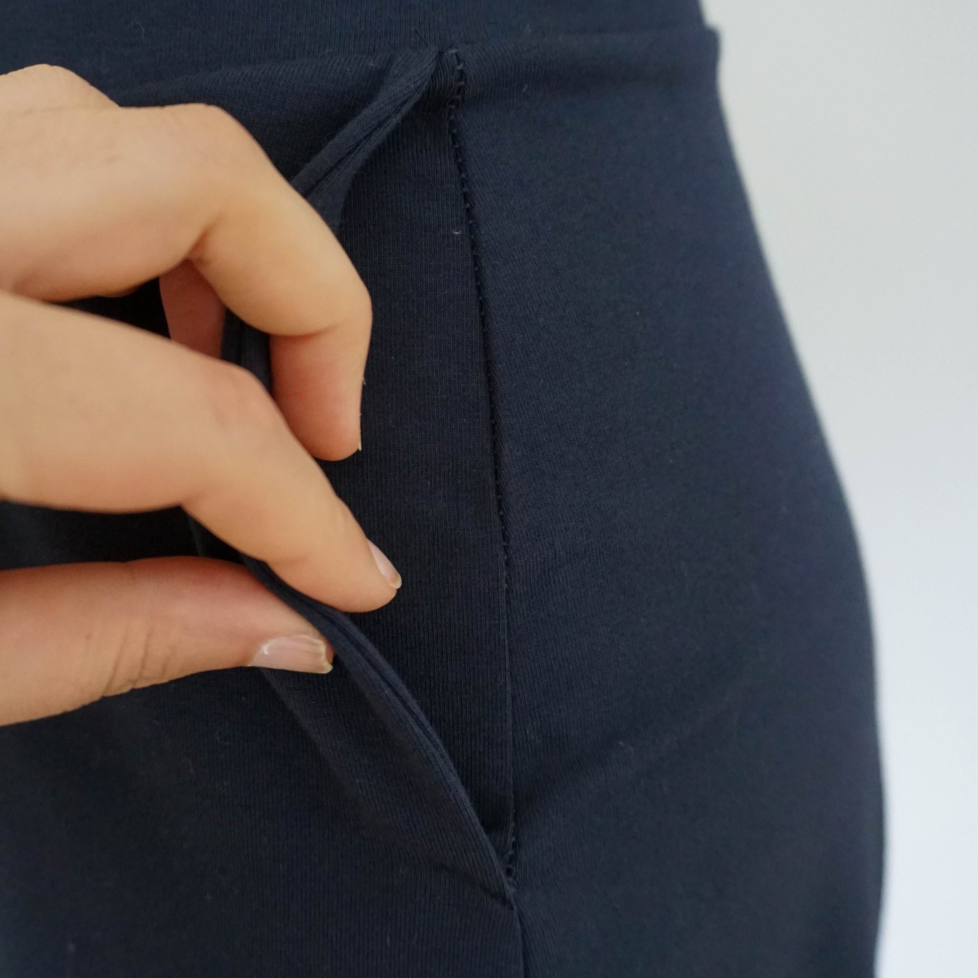 A close-up of a dark blue cuffed baggy pant pocket, with a hand pulling it open to reveal its interior stitching.