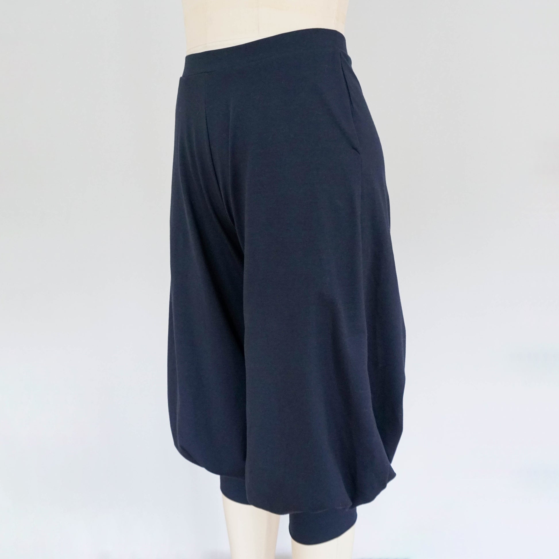 A side view of dark blue cuffed baggy pants displayed on a mannequin, showcasing the loose fit, side pocket, and gathered ankle cuffs.