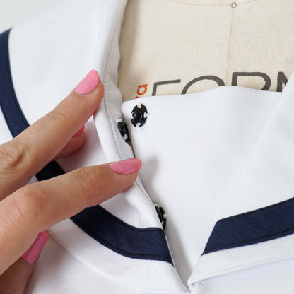 Close-up of a hand with pink nail polish near the collar of a white seifuku. The collar has navy blue trim and black snap closures. The image highlights the details of the garment's construction and design.