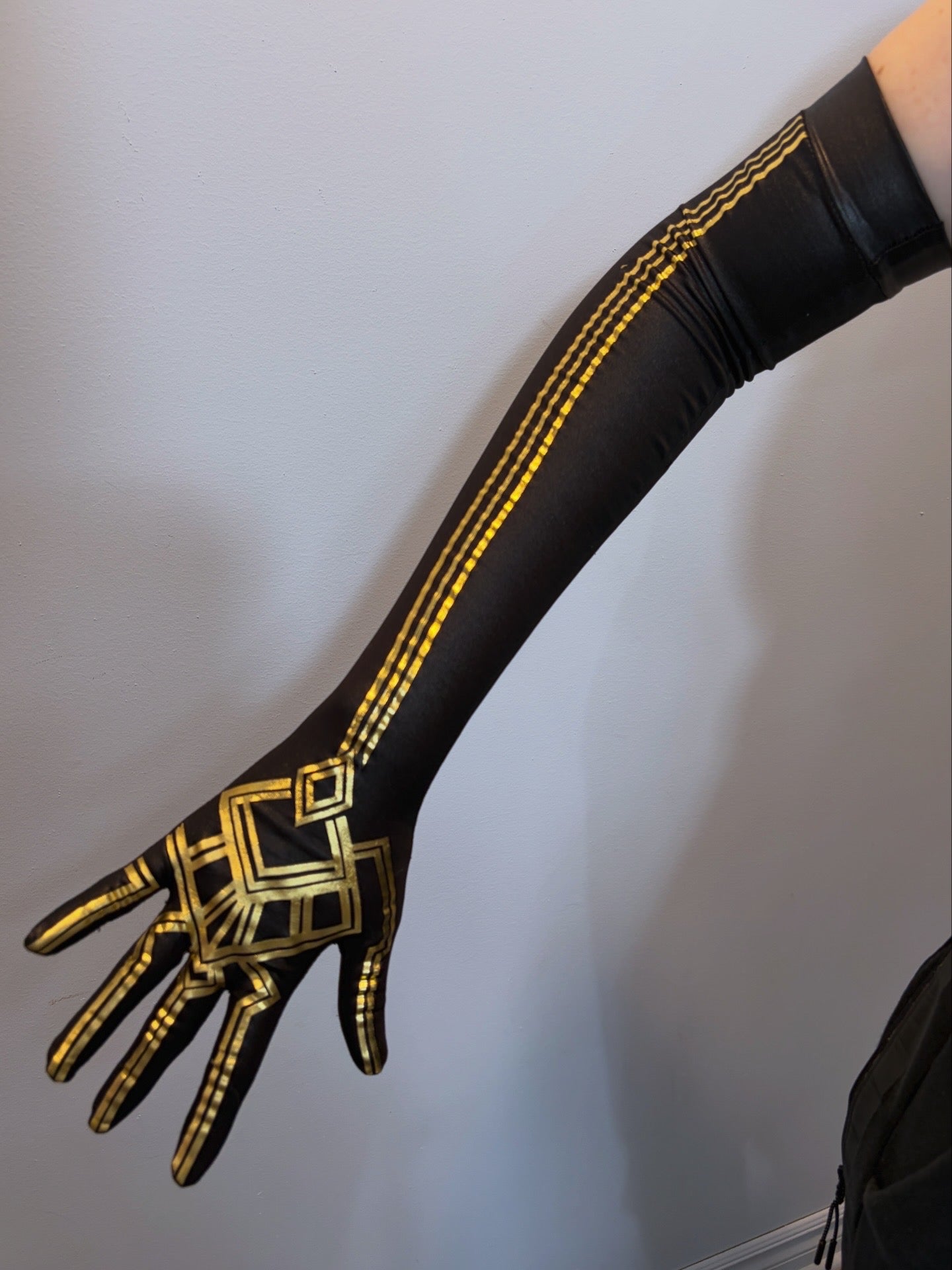 A long black stretch glove worn on an outstretched arm. Features gold geometric HTV detailing running along the back of the hand and up the forearm, including a square motif on the hand and parallel stripe accents along the arm.