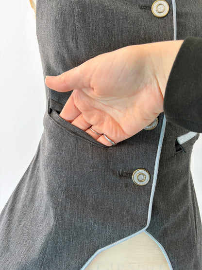 Close-up of a hand slipping inside the open welt pocket of the Structured Fitted Vest, showing the pocket depth and clean interior finish. Light blue piping trims the curved hem below.