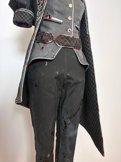 Lower body detail of a cosplay costume on a dress form. Shows the asymmetrical hem of the quilted black coat with red trim, the curved bottom edge of the grey vest, a quilted dark red belt with scalloped edges, black cropped pants with blood splatter distressing, and the short quilted sleeve with a purple lining visible at the cuff.