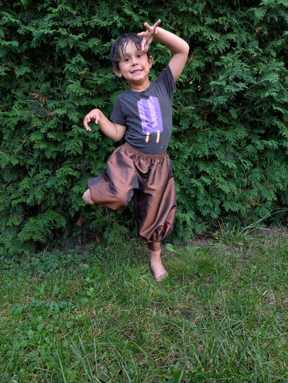Child playfully posing outdoors in handmade satin baggy pants.