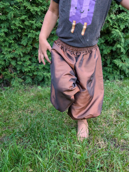 Close-up of handmade satin baggy pants worn by a child outdoors.